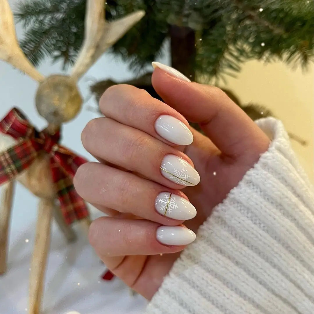 Witte ovale nagels met sneeuwvlokdessins en gouden accenten bij hoe lak je je nagels zonder ze te beschadigen