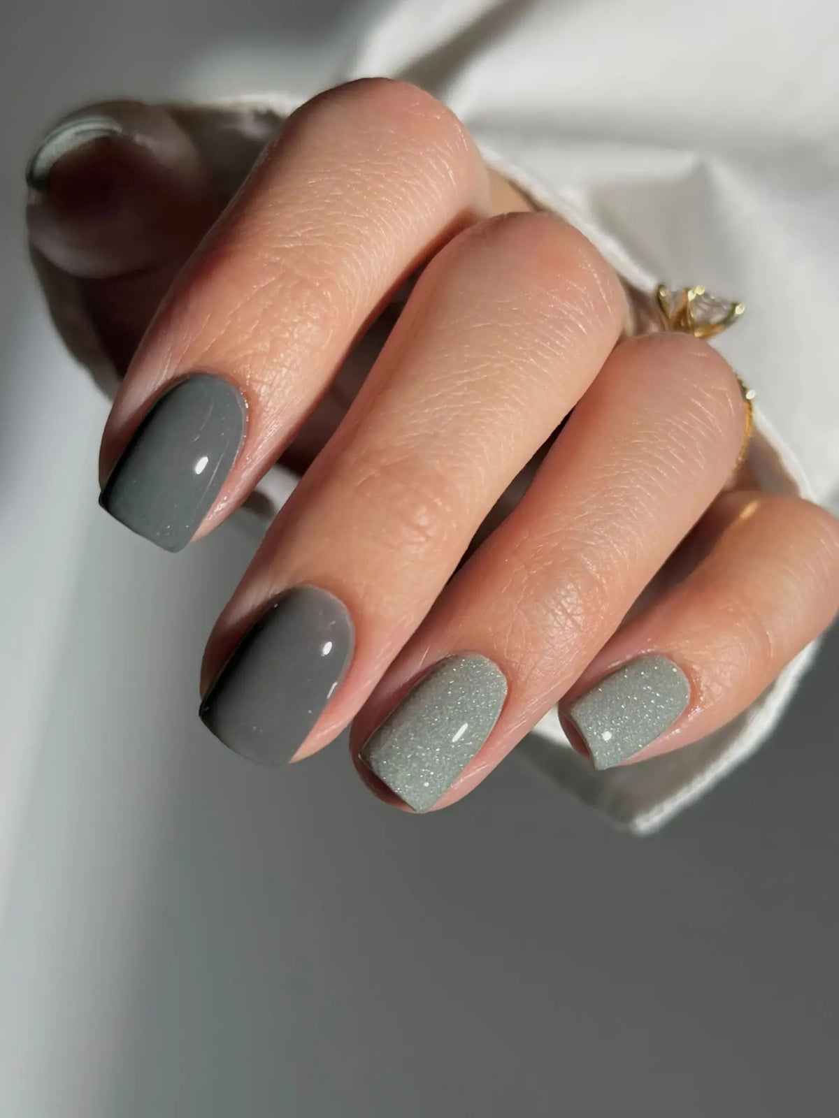 Hand met verzorgde nagels in grijze nagellak met twee matte en een glitterende tint voor minder schadelijke nagels