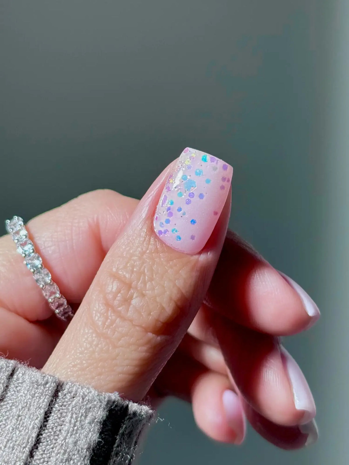 Hand met nagel gelakt in zachtroze met blauwe en paarse glitterdruppels voor een gezond nageladvies