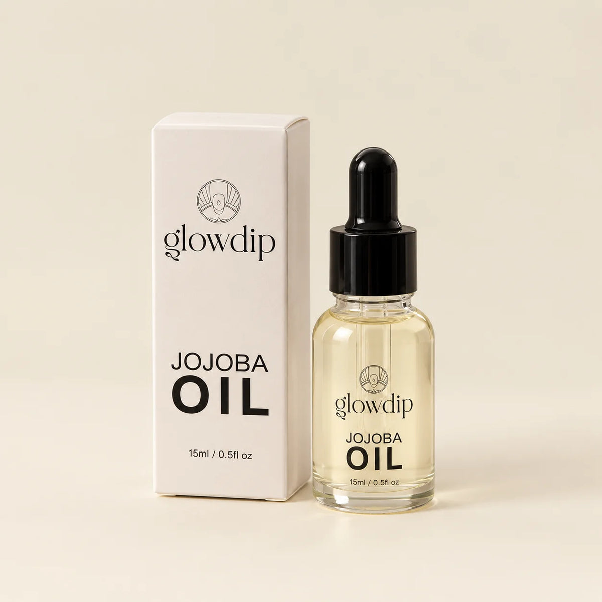 Een heldere glazen fles met zwarte druppelpipdop gevuld met goudgele glowdip jojobaolie naast witte doos jojoba nagelriemolie