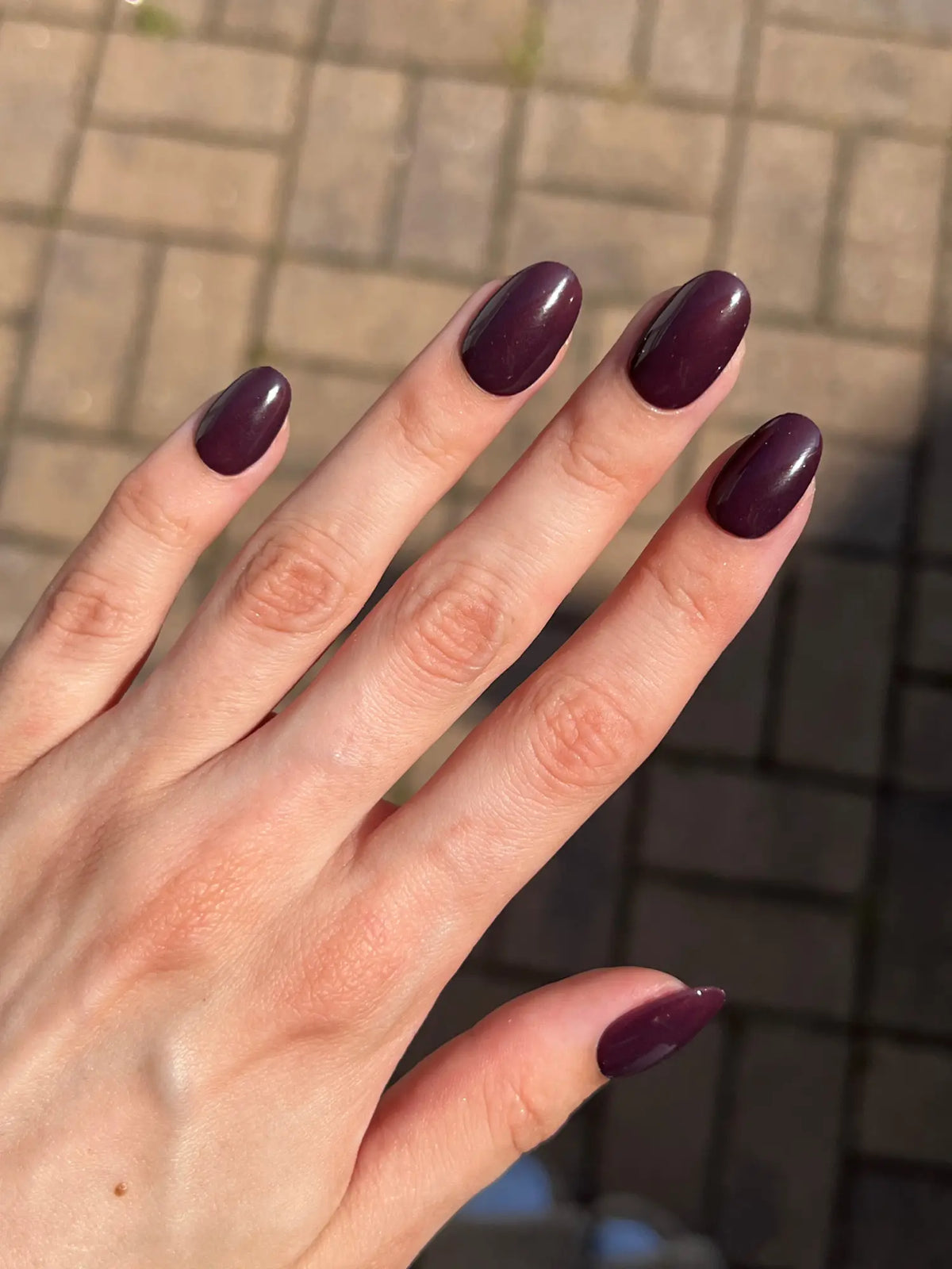 Een hand met langwerpige ovale nagels gelakt in glanzend diep bordeauxrood bij symptomen van dip flu