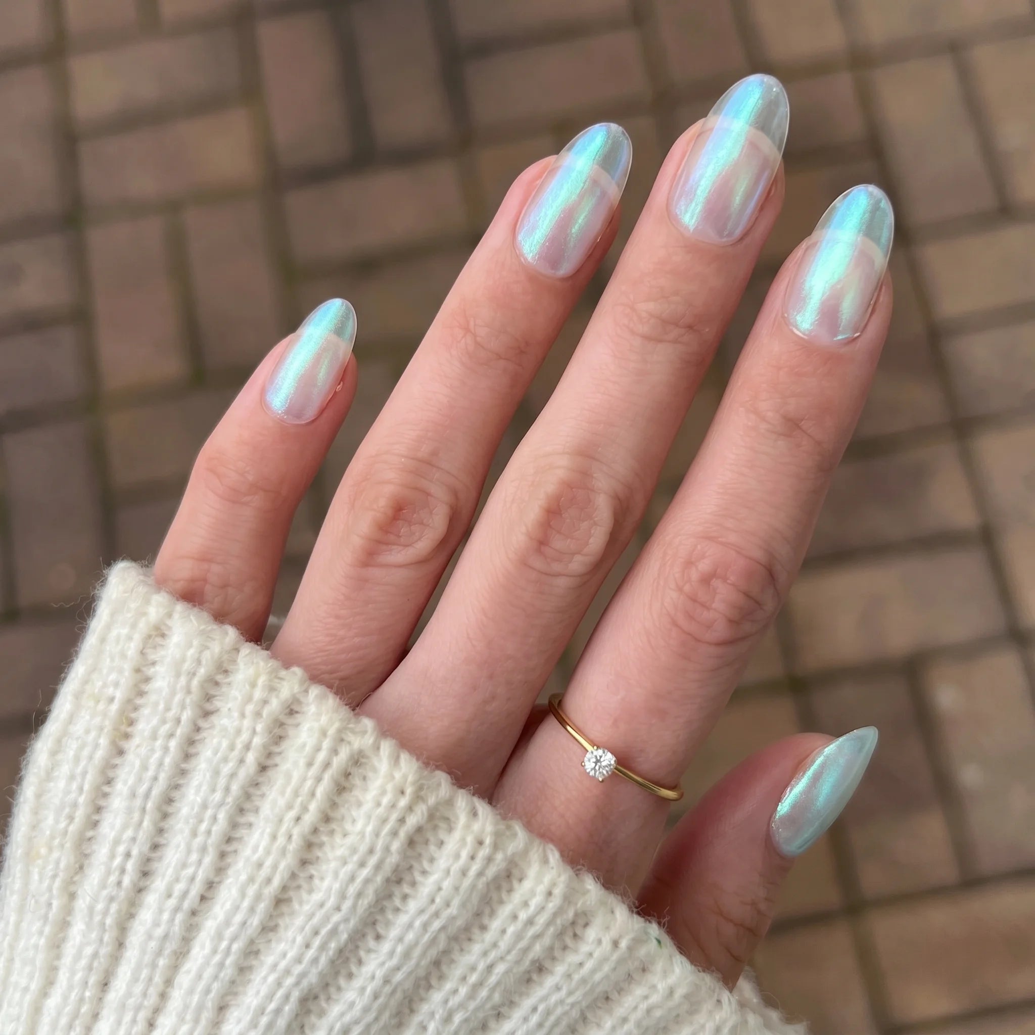 Hand met lange amandelvormige nagels met een glinsterende iriserende lichtblauwe en witte holografische manicure met crimson shift chrome powder